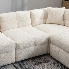 a white sectional couch with pillows on top of it in a living room next to a rug