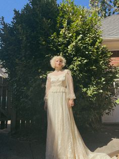 a woman standing in front of a tree wearing a white wedding dress with long sleeves