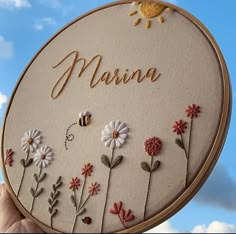 a person holding up a embroidery kit with flowers and bees on it that says marina