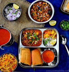 an assortment of food is displayed on a blue tablecloth with silver bowls and spoons