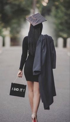 a woman walking down the street with a graduation cap on her head and holding a black bag