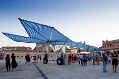 a group of people standing around a large blue umbrella on top of a parking lot