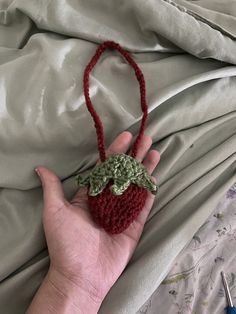 a hand holding a crocheted strawberry ornament on top of a bed