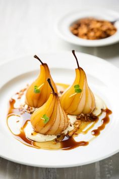 two pears are sitting on a white plate with caramel sauce and nuts in the background