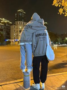 a person standing on the sidewalk with their back turned to the camera and holding onto a skateboard