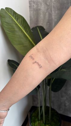 a woman's arm with the word love written on it and a plant behind her