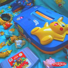 a blue and yellow nintendo game system sitting on top of a bed next to other toys