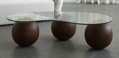 a glass coffee table with two brown balls on the bottom, and a white couch in the background