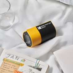 a yellow and black speaker sitting on top of a bed next to an open book