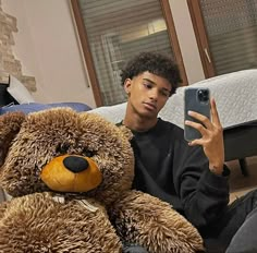 a young man sitting on the floor next to a teddy bear holding a cell phone