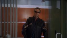 a man standing in front of a glass door wearing sunglasses and a black leather jacket