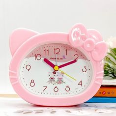 a pink hello kitty alarm clock sitting on top of a table next to some books