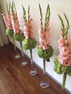 four tall vases filled with pink and green flowers on top of a wooden floor