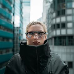 a woman wearing glasses standing in front of tall buildings