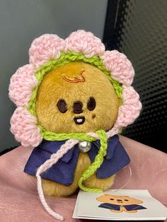 a teddy bear wearing a crocheted hat and scarf on a pink table cloth