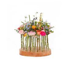 a bunch of flowers that are in a vase on a wooden stand with some grass