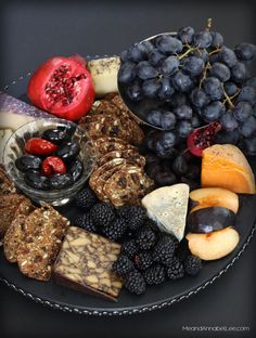 a plate full of cheeses, crackers, fruit and other foods on it