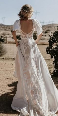 a woman standing in the desert wearing a white dress with sheer sleeves and an open back