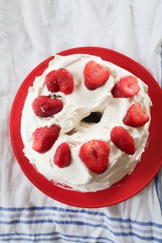 a cake with white frosting and strawberries on top sitting on a red plate