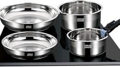 three stainless steel pots and pans sitting on top of a black stove with an electric toothbrush