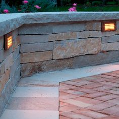 an outdoor fire pit with two lights on it's sides and brick pavers