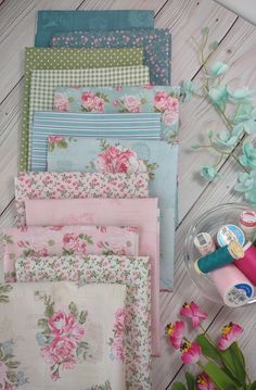 several different types of fabric on a table with flowers and sewing supplies next to them