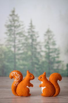 two small squirrel figurines sitting next to each other on a wooden table with trees in the background