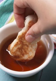 a person dipping something into a bowl of soup with a small piece of bread sticking out of it