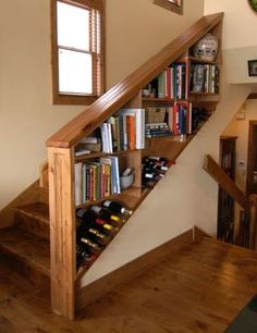 there is a book shelf with many books on it and wine bottles under the stairs