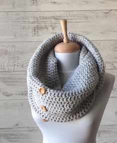 a white mannequin head wearing a gray crochet cowl scarf with buttons