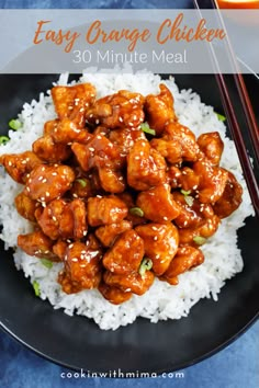 a black plate topped with chicken and rice next to oranges, chopsticks and an orange