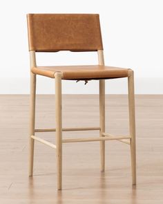 a brown leather bar stool sitting on top of a hard wood floor next to a white wall