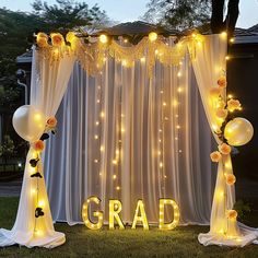 an arch decorated with lights and balloons for graduation party decorations in front of a white curtain