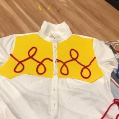 a white shirt with yellow and red thread on the collar is sitting on a wooden floor