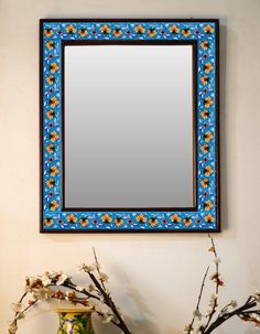 a blue and yellow mirror sitting on top of a table next to a vase with flowers