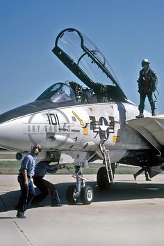 a fighter jet sitting on top of an airport tarmac with two men standing next to it