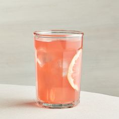 a glass filled with pink liquid sitting on top of a white table next to a slice of lemon