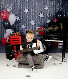 a young child sitting on top of a stool holding a guitar in front of a party backdrop