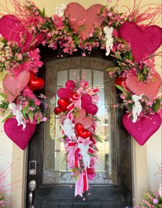 a valentine's day wreath with pink flowers and heart shaped decorations on the front door