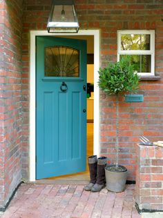 a blue front door with potted plants on the side and brick walkway leading up to it