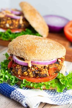 two burgers with lettuce, tomato and onion on them sitting on a napkin