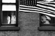 an american flag hanging from the side of a brick building next to two windows with mannequins in them