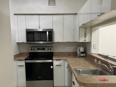 an empty kitchen with stainless steel appliances and white cupboards, counter tops, and tile flooring