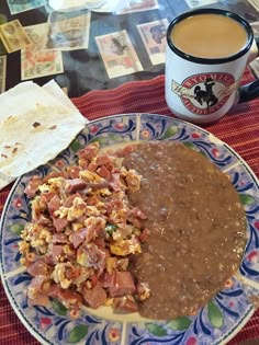 a plate with beans, rice and meat on it next to a cup of coffee