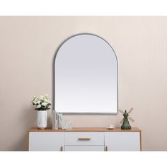 an arched mirror on a wall above a dresser with vases and flowers next to it