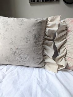 three pillows on top of a bed with white sheets and ruffled trimmings