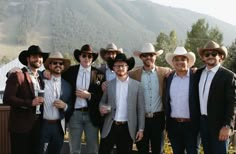 a group of men standing next to each other wearing cowboy hats and sunglasses on top of a roof