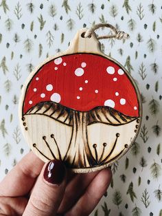 a hand holding a wooden ornament with a red mushroom on it's side