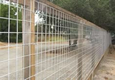 the fence is made of metal wire and has wood posts on each side, along with gravel