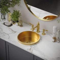 a bathroom sink with gold faucet and marble counter top, surrounded by greenery